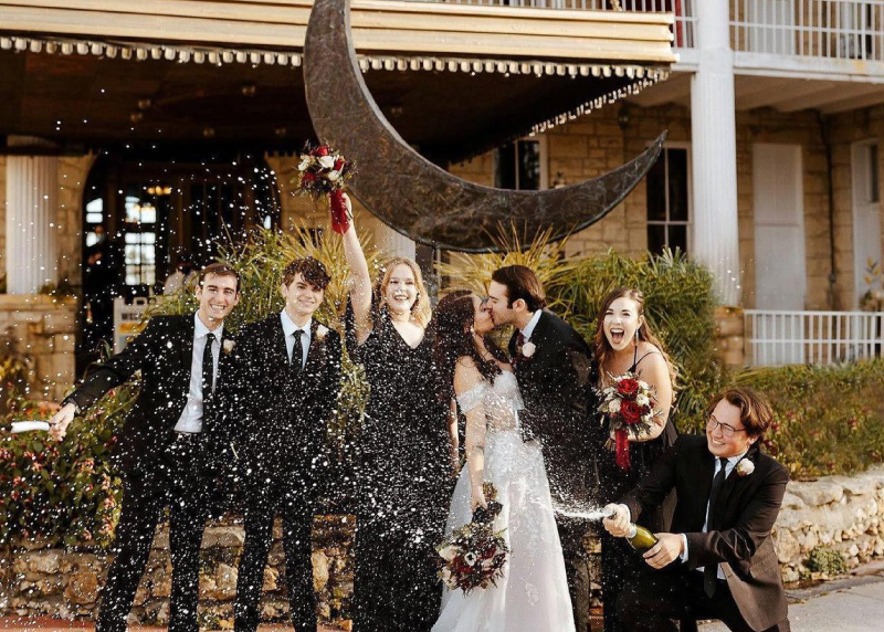 Bride and groom kissing with groomsmen throwing champagne while standing in front of Crescent Hotel